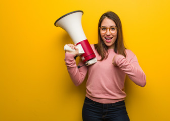 Young cute woman holding a megaphone surprised, feels successful and prosperous