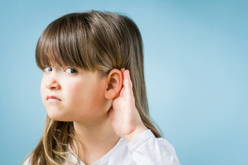 Toddler girl with hearing problem on light blue background. Close up, copy space.