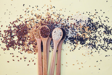 wooden spoons with assorted seeds isolated on yellow background, chia, linen sesame, healthy food...