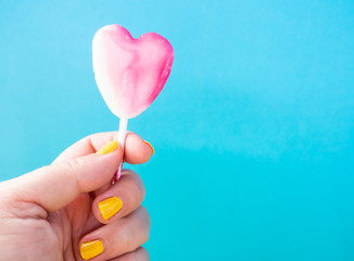 A woman with yellow painted nails with a lollipop in her hand and blue background