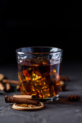 Glass of brandy or whiskey, spices and decorations on dark background. Seasonal holidays concept.