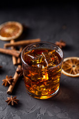 Glass of brandy or whiskey, spices and decorations on dark background. Seasonal holidays concept.