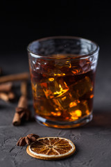 Glass of brandy or whiskey, spices and decorations on dark background. Seasonal holidays concept.