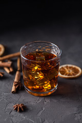 Glass of brandy or whiskey, spices and decorations on dark background. Seasonal holidays concept.