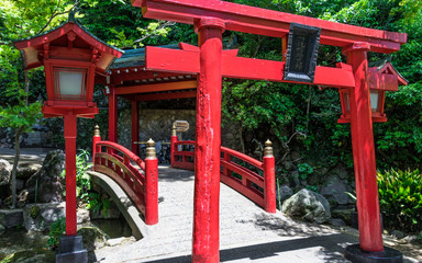 Traditional red Bridge, Lantern and Torii to japanese Jigoku Meguri Shinto Shrine framed by a green landscape. In Beppu, Oita Prefecture, Japan, Asia.