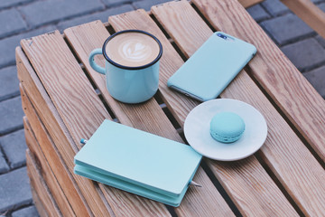 blue cup of coffee and book and phone and macaroon on wooden table