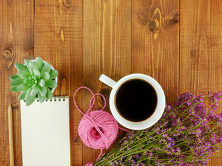 Flat lay,top view brown wooden desk with stationery including notebook and pencil with a cup of coffee,flowers and copy space