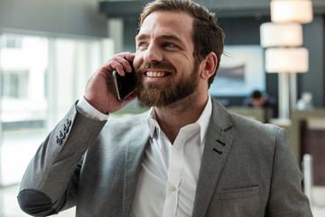 Smiling businessman talking on smart phone while standing in hotel lobby
