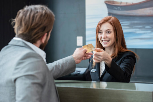 Businessman giving credit card to smiling female receptionist while standing at hotel reception desk