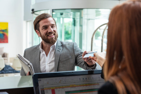 Female receptionist giving credit card to smiling businessman while standing at hotel reception desk