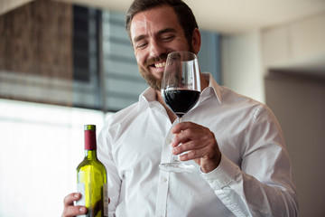 Smiling mid adult man holding wine bottle and glass in bar