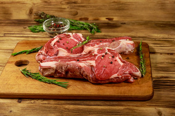 Raw fresh beef rib eye steaks on bone with spices and rosemary on wooden table