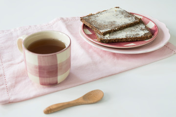 rye bread, Dutch roggebrood, on pink plate. Cup of tea and pink napkin, on white table