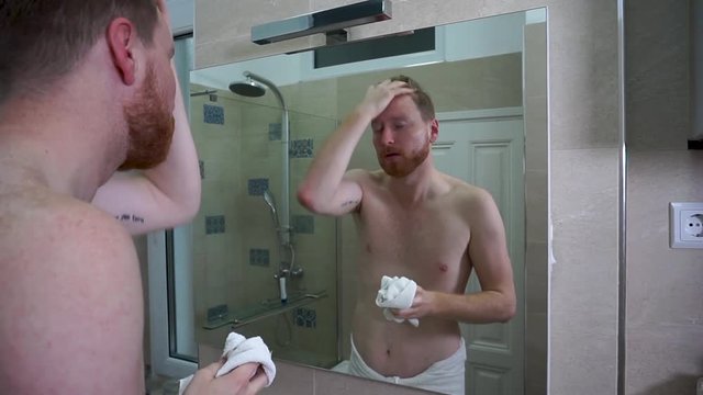 Young caucasian man drying his face with a little white face towel in the bathroom