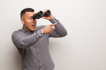 Latin man pointing to the side with finger. He is holding a binoculars.