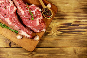 Raw fresh beef rib eye steak on bone with spices, garlic and rosemary on wooden table. Top view