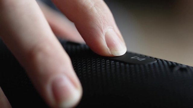 Close up of finger pressing power button to a speaker