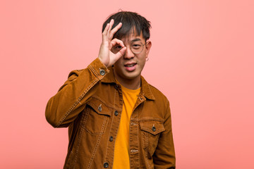Young chinese man wearing a jacket confident doing ok gesture on eye