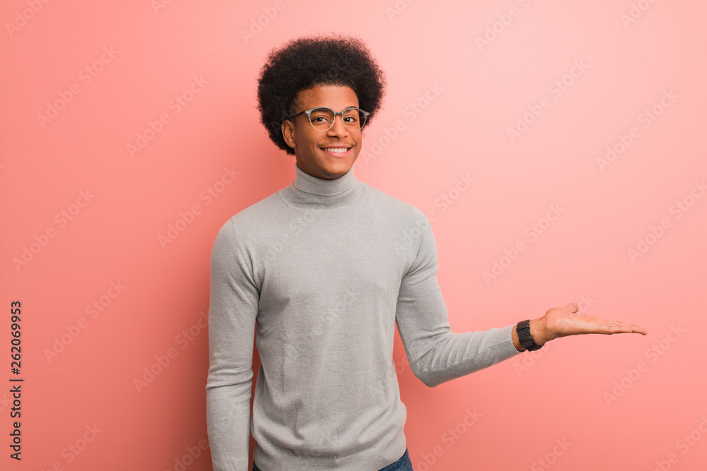 Wall mural Young african american man over a pink wall holding something with hand