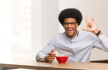 Fototapeta na wymiar Young black man having a breakfast doing a rock gesture