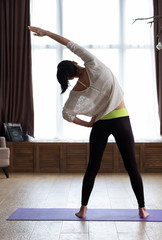 Slim young woman stretching against a white window