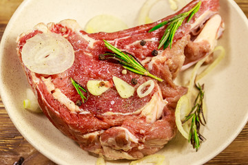 Marinated beef rib eye steak on bone with spices, onion and rosemary on wooden table