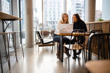 Female students working on common homework project at modern coffee shop