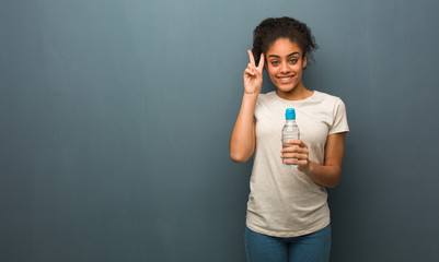 Young black woman fun and happy doing a gesture of victory. She is holding a water bottle.