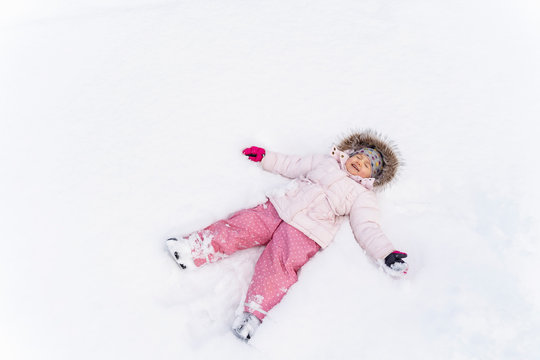 Cute little girl lying in snow in winter making a snow angel