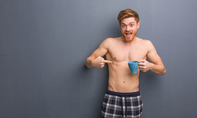 Fototapeta na wymiar Young shirtless redhead man surprised, feels successful and prosperous. He is holding a coffee mug.