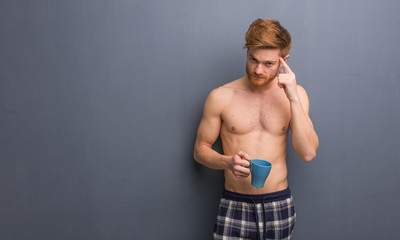 Obraz premium Young shirtless redhead man thinking about an idea. He is holding a coffee mug.