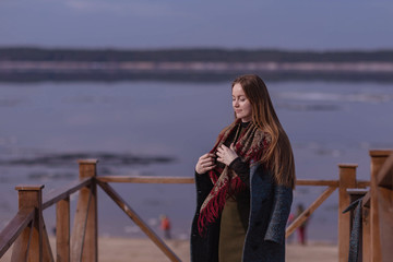 a girl in a coat on the site with a railing on the background of the Volga river with floating ice...