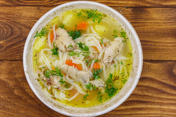 Chicken soup with noodles and vegetables on wooden table. Top view