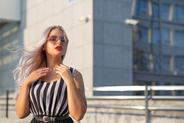 Fototapeta premium Attractive blonde girl with fluttering hair wearing glasses posing at the street. Empty space