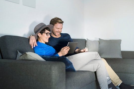 Happy casual couple relaxing on couch using tablet