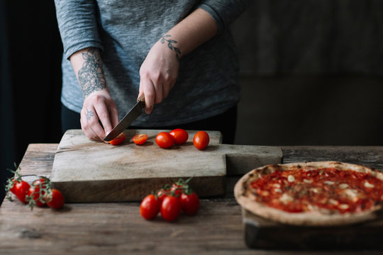 Young woman preparing pizza, cutting tomatoes on chopping board