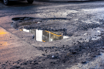 Asphalt road in city with a huge pit and puddle