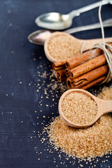 Brown cane sugar, cinnamon sticks and star anise closeup on black board background.