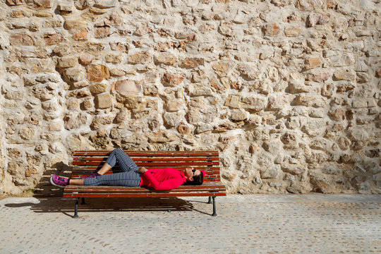 A female runner rests on a bench in the medeival old town section of Cuenca, Spain. The area is a UNESCO World Heritage Site and popular tourist destination.