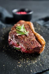 Poster Beef ramp steak with rosemary. Black background, top view. © Vladimir