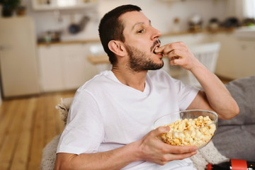 Fototapeta na wymiar Man eating popcorn while watching TV alone at home. The concept of bachelor life man