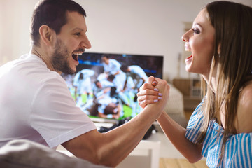 Couple watching soccer game on television, celebrating goal screaming taking five and hugging