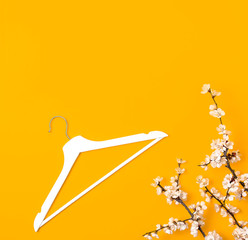Creative fashion beauty background. White wooden hanger and spring flowering branch on yellow background. Spring sale concept discount store shopping empty hanger promo design. Flat lay top view