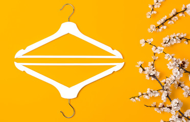 Creative fashion beauty background. White wooden hangers and spring flowering branch on yellow background. Spring sale concept discount store shopping empty hanger promo design Flat lay top view