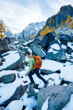 A man with a pack scrambles up a rocky ridge amidst fall colors near Colchuck Lake in the Cascade Range of Washington State.