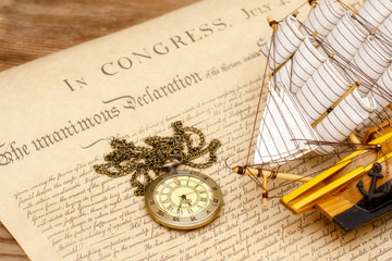 Ship made of wood and fabric handmade and vintage watches on the background of an excerpt from a copy of the document of 1776 on the signing of the independence of America