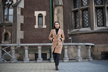 Young beautiful woman with long brown hair in sunglasses on a walk on a cloudy day. Fashionable sexy girl. Street fashion look. Cute student.