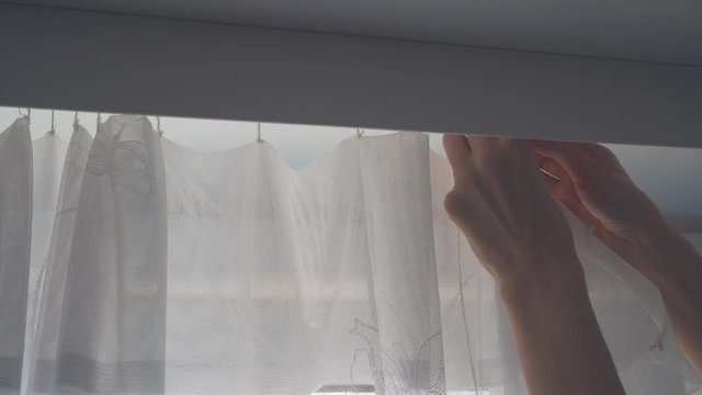 women's hands take the curtain off the hooks, the tulle is removed from the cornice for washing. The process of cleaning the apartment.