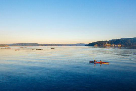 Two tandem kayakers paddle into the early morning light near Harney Channel while on a 3-day sea kayaking trip in the San Juan Islands. The photo was taken from Blind Island, a small 3 acre state park near Shaw Island that offers camping opportunities to human and wind-powered boats.