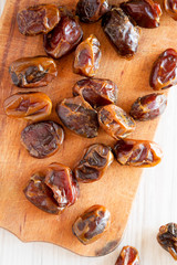 Dried dates on rustic wooden board over white wooden surface, top view. From above, overhead, flat lay. Close-up.